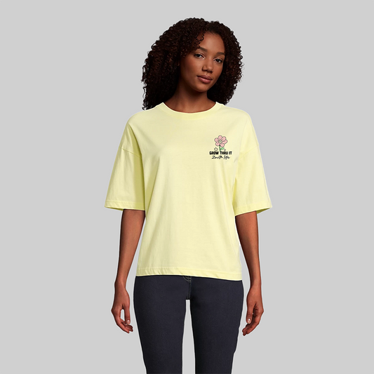 Modelo femenina con camiseta amarillo pastel Boxy Fit de algodón orgánico Zouth Life con logo frontal "Grow Thru It".