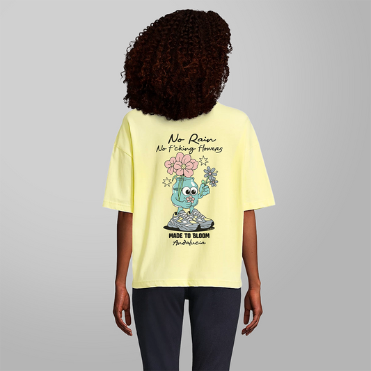 Chica de espaldas con camiseta boxy amarilla clara de Zouth Life mostrando diseño "No Rain, No Flowers" con flores y zapatillas.