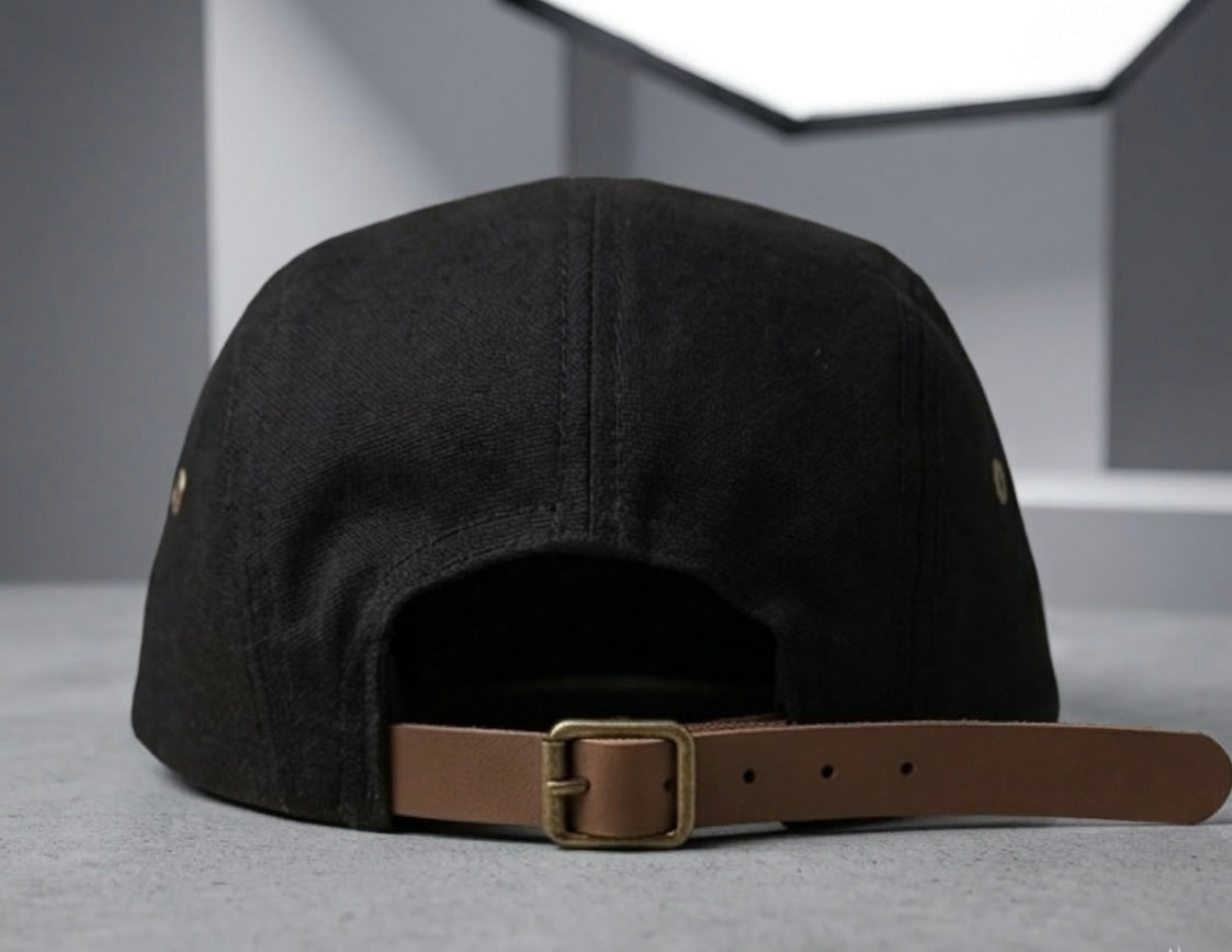 Vista posterior de gorra "5-panel" negra que muestra el cierre ajustable de correa de cuero marrón con hebilla metálica de latón envejecido