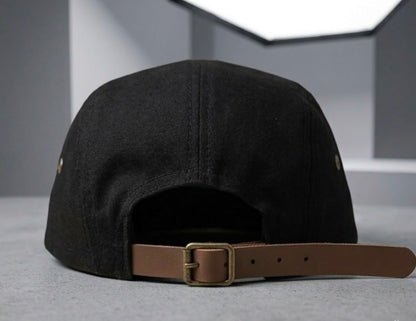 Vista posterior de gorra "5-panel" negra que muestra el cierre ajustable de correa de cuero marrón con hebilla metálica de latón envejecido