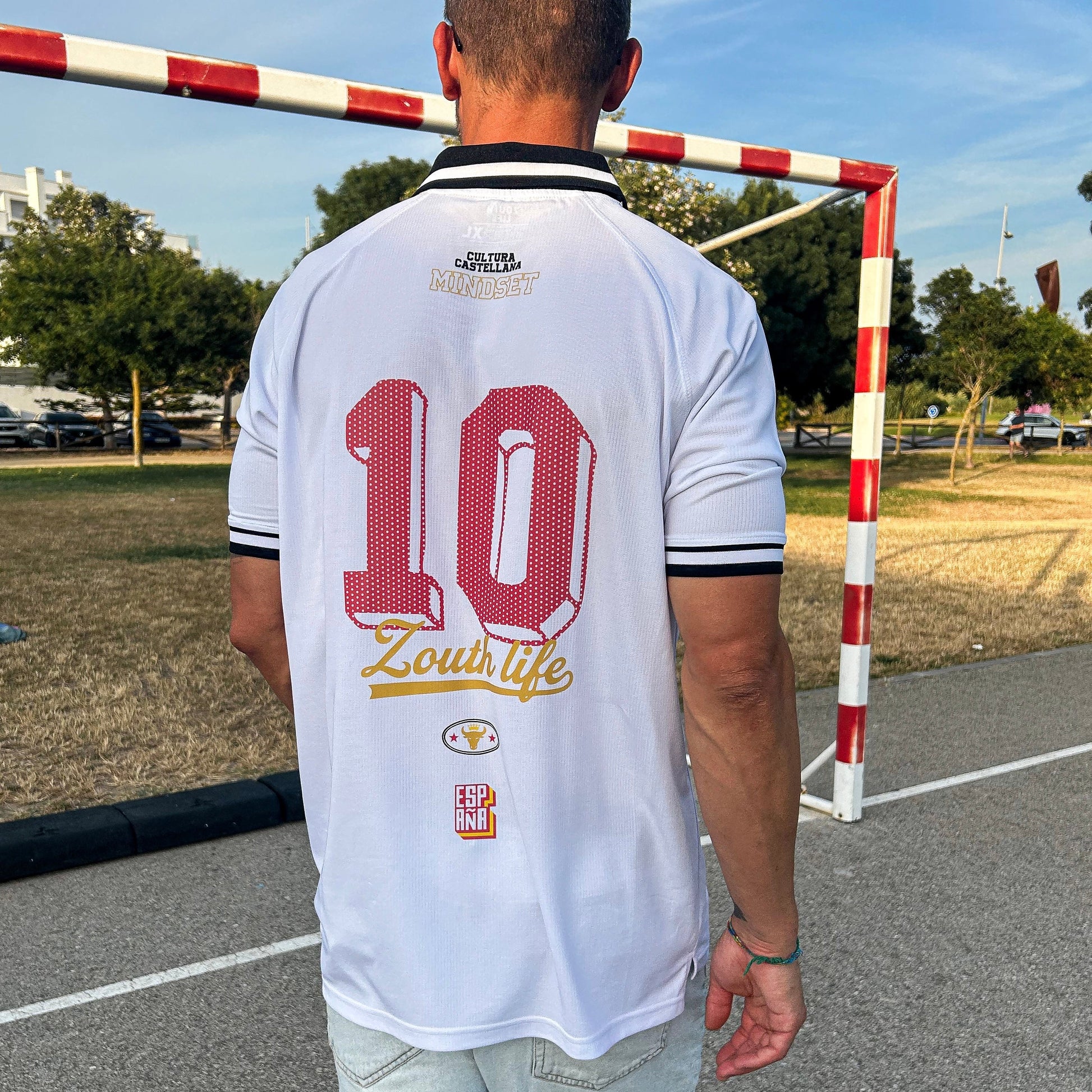 Vista trasera del polo retro de España de Zouthlife con el dorsal 10 en color rojo, tipografía de estilo noventero y logotipo dorado Cultura Castellana en una pista exterior.