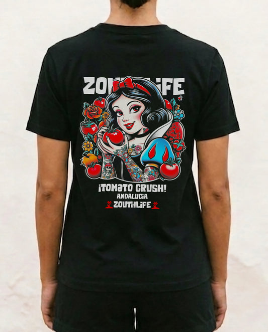 Vista trasera de una persona vistiendo la camiseta negra de corte regular fit Blanca Nieves de Zouth Life. El diseño trasero muestra una ilustración de estilo tatuaje de Blanca Nieves con los brazos tatuados, sosteniendo un tomate rojo en lugar de una manzana, rodeada de flores y tomates. En la parte superior se lee 'ZOUTHLIFE' y abajo el texto '¡TOMATO CRUSH! ANDALUCIA ZOUTHLIFE', sobre un fondo de pared blanca texturizada.