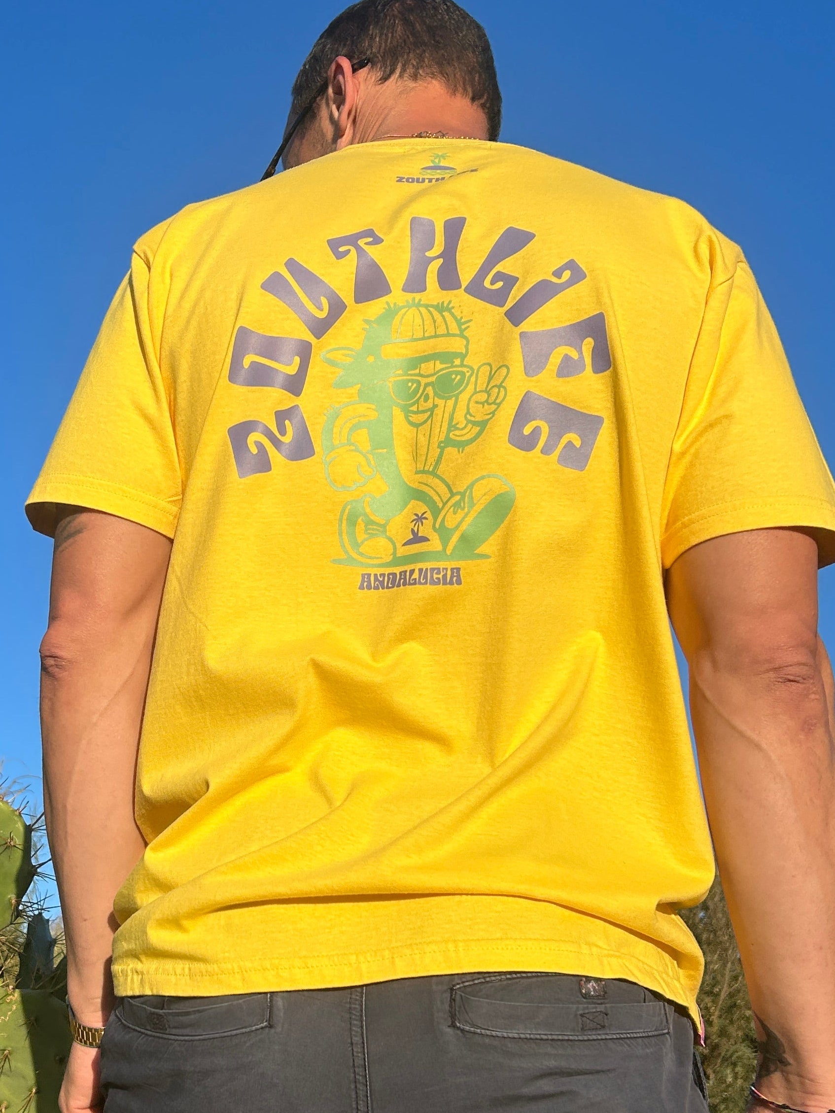 Modelo luciendo Camiseta Amarilla Zouth Life con diseño de cactus verde y texto morado estampado en espalda.