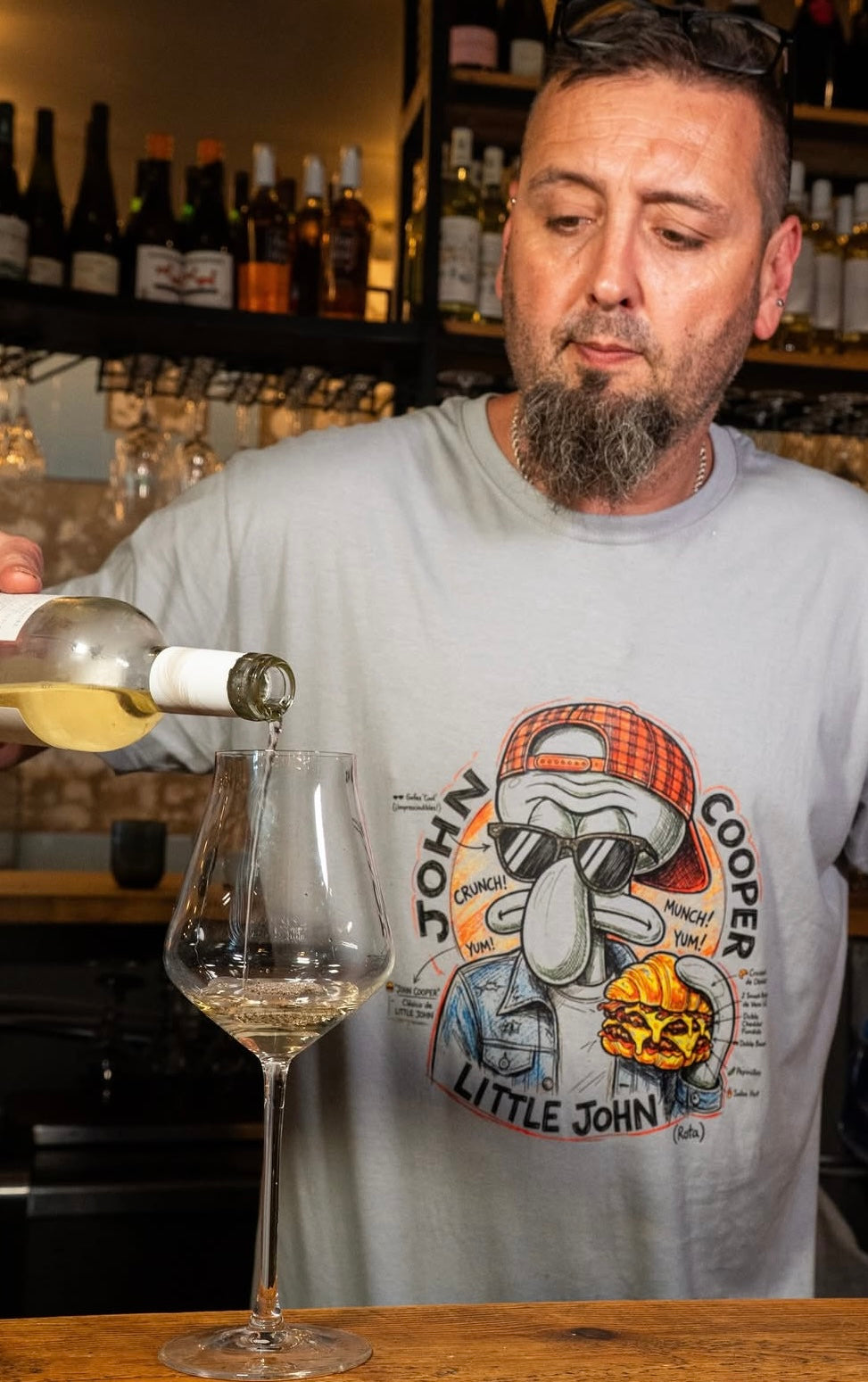 Camiseta gris John Cooper de Zouthlife: imagen lifestyle en restaurante  donde se aprecia el diseño gráfico retro inspirado en personajes de animación y cultura gastronómica de Rota. Ropa urbana de corte relajado para hombre.