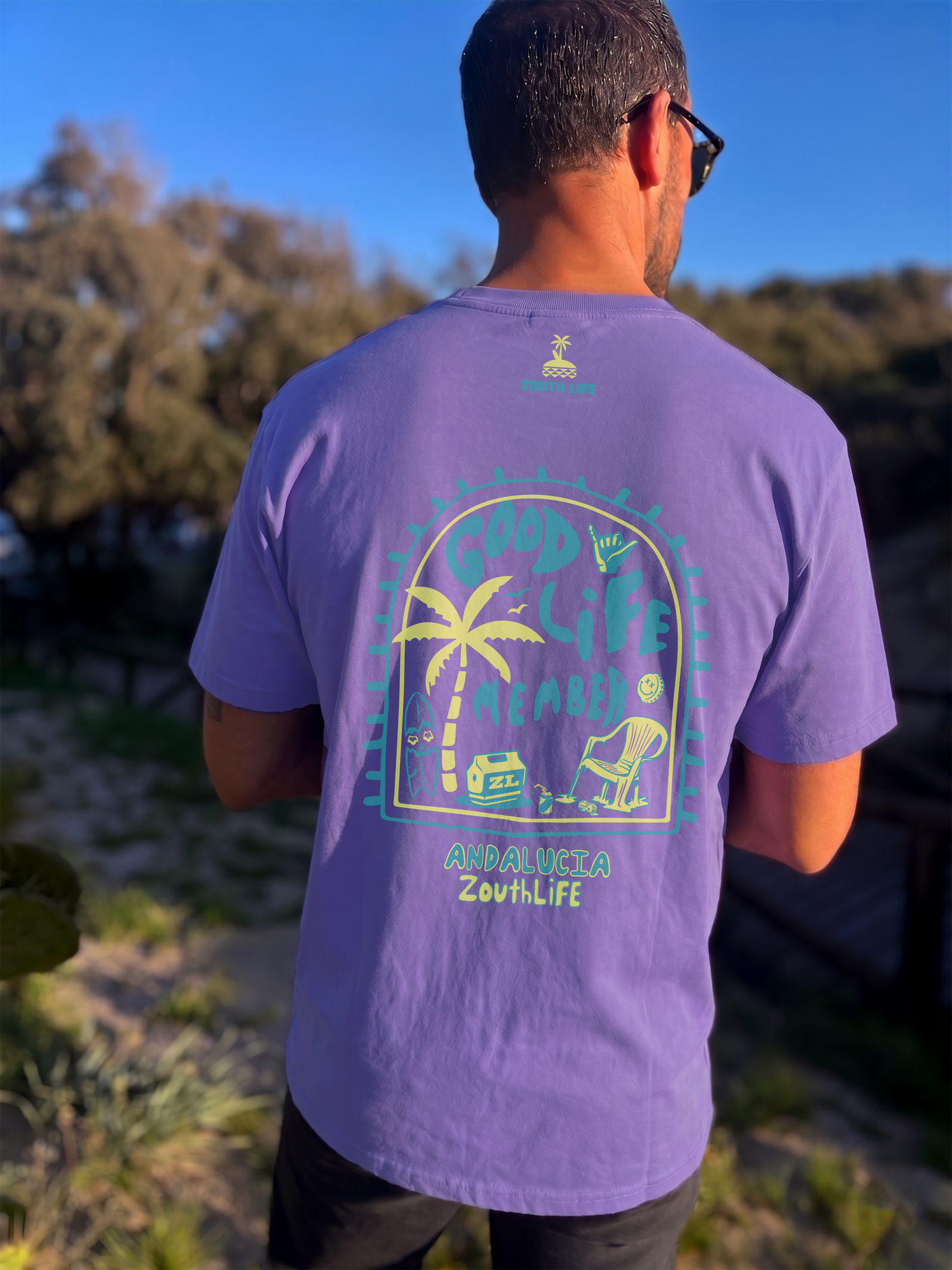 Modelo luciendo camiseta lavanda con estampado de Zouth Life en Andalucía. Diseño gráfico playero 'Good Life Member' , capturado en exteriores con iluminación natural de alta calidad